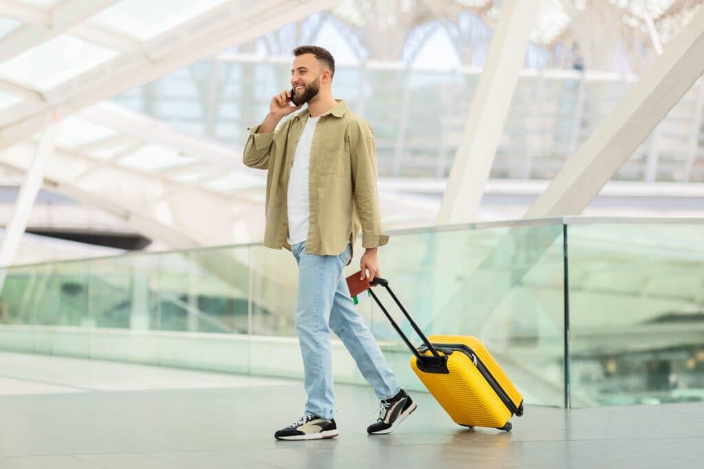 Ein Mann mit einem Rollkoffer und Reisepass als auch Flugticket geht durch einen Flughafen